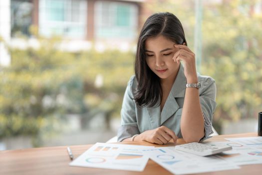 Thoughtful asian woman managing budget and finances using calculator in office, financial accounting concept
