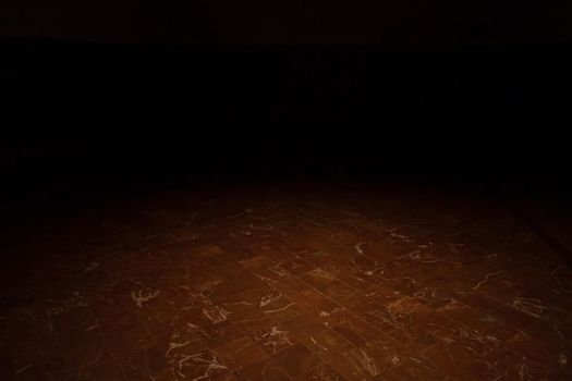 A very dark room with a spotlight on the red marble floor