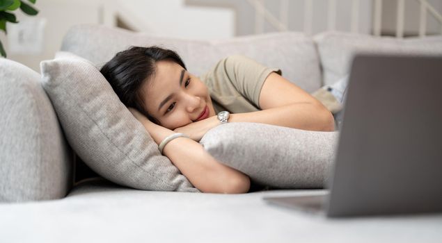 beauty asian woman watch video tv series on laptop computer happily on the bed at home.