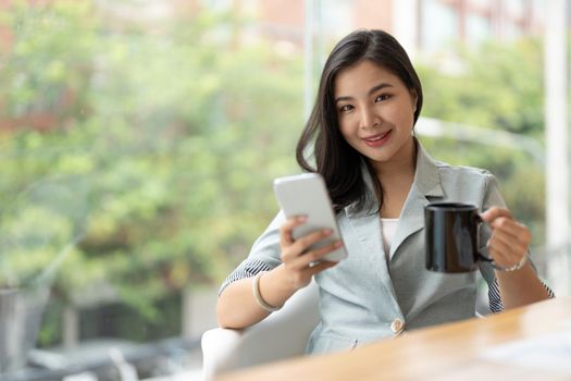 Smiling asian businesswoman using phone in office. Small business entrepreneur looking at her mobile phone and smiling