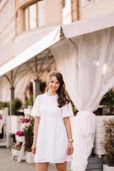 A beautiful woman in a white dress at sunset in the city. Evening street photography.