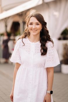 A beautiful woman in a white dress at sunset in the city. Evening street photography.