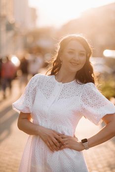 A beautiful woman in a white dress at sunset in the city. Evening street photography.