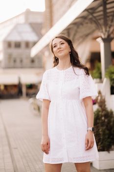 A beautiful woman in a white dress at sunset in the city. Evening street photography.