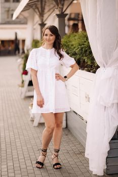 A beautiful woman in a white dress at sunset in the city. Evening street photography.