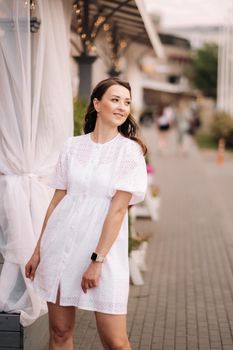 A beautiful woman in a white dress at sunset in the city. Evening street photography.