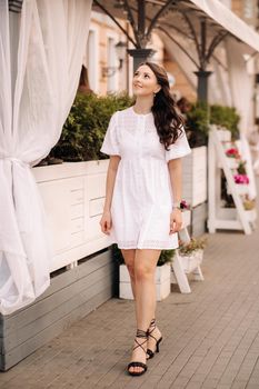 A beautiful woman in a white dress at sunset in the city. Evening street photography.