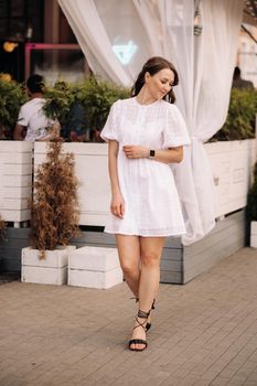 A beautiful woman in a white dress at sunset in the city. Evening street photography.