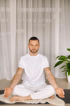 a man in white sportswear is doing yoga with a fitness room. the concept of a healthy lifestyle.