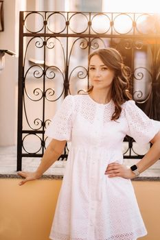 A beautiful woman in a white dress at sunset in the city. Evening street photography.