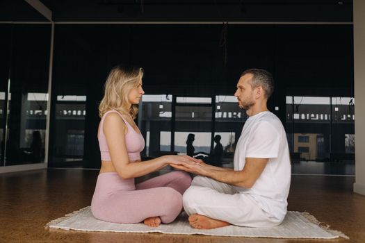 a woman and a man are engaged in pair meditation holding hands in the gym.