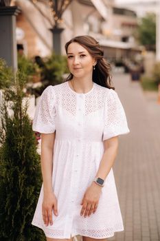 A beautiful woman in a white dress at sunset in the city. Evening street photography.