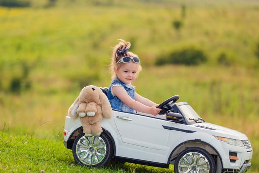 little girl rides on a children's car on a green lawn