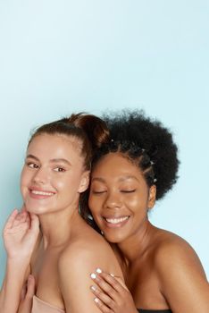 Portrait of two wonderful multiethnic women on blue background. Beautiful women, flawless skin. Diverse friends