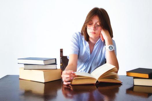 A white caucasian young teen student sitting at a table reading books looking bored