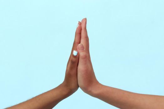 Hands of Caucasian and black African American women giving each other five on blue background. The concept of racism and all lives matter.