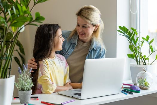 Happy mother with little kid daughter having fun online with application, watching video cartoons or playing game on laptop together, young babysitter or nanny teaching child girl to use computer.