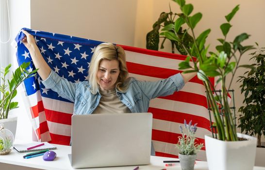 Happy young female student hold flag of USA, studying with laptop with blank screen in living room interior. International education at home, lesson remote, website due covid-19 quarantine.