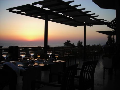 Interior view of the bar-restaurant at sunset. Sea and beautiful sunset. The image of the open terrace of the restaurant at sunset on a warm summer evening over the sea. Vacation and travel concept.