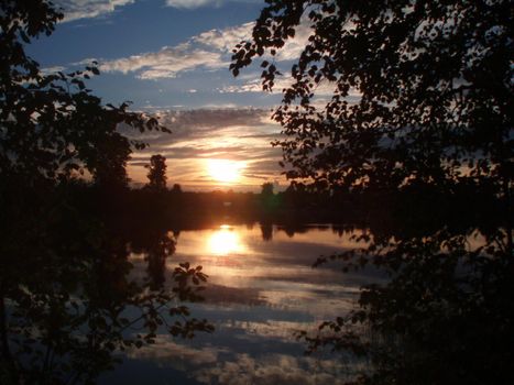 Beautiful sunset on the lake. Sunset reflected in the water - blue and orange sky with clouds and trees in silhouette.