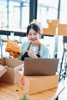 Portrait of a small startup business, SME owner, Asian female entrepreneur, talks to via video conferance, lets customers see products before pricing and packing them into boxes. Online Business.