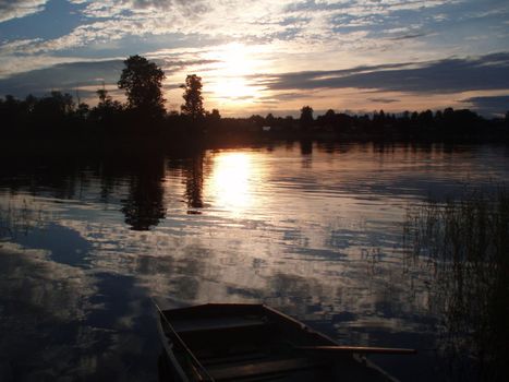 Beautiful sunset on the lake. Sunset reflected in the water - blue and orange sky with clouds and trees in silhouette. boat on the lake