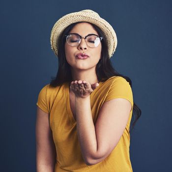 Studio portrait of an attractive young woman blowing a kiss against a blue background.