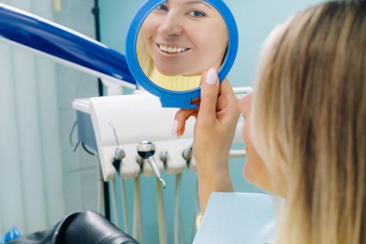 The girl smiles and looks in the mirror in dentistry.