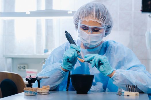 A dental technician in protective clothing is working on a prosthetic tooth in his laboratory.