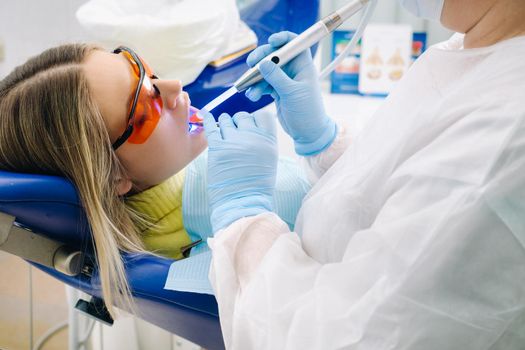 A young beautiful girl in dental glasses treats her teeth at the dentist with ultraviolet light. filling of teeth.