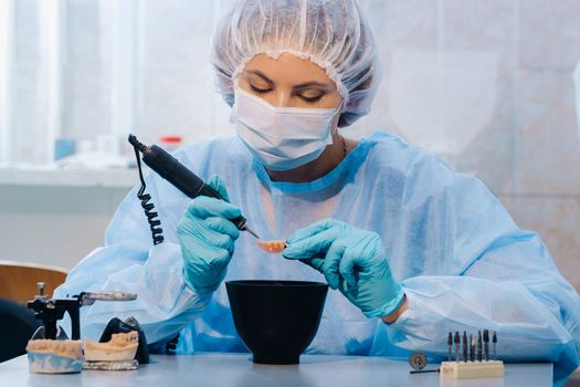 A dental technician in protective clothing is working on a prosthetic tooth in his laboratory.