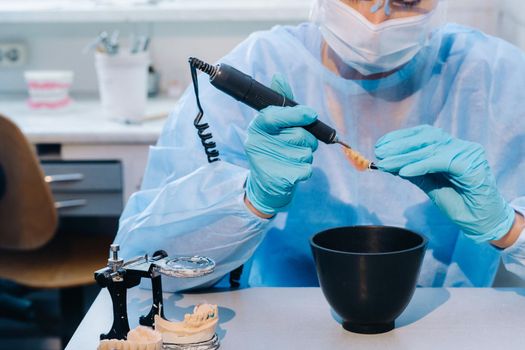 A dental technician in protective clothing is working on a prosthetic tooth in his laboratory.