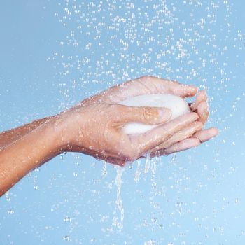 Studio shot of an unrecognisable woman holding a bar of soap while taking a shower against a blue background.