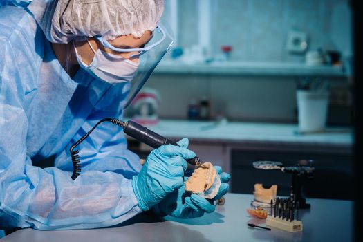 A dental technician in protective clothing is working on a prosthetic tooth in his laboratory.