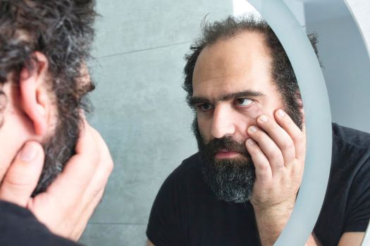 Middle-aged man looking tired and depressed in the bathroom mirror