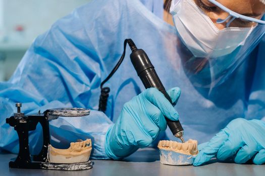 A dental technician in protective clothing is working on a prosthetic tooth in his laboratory.