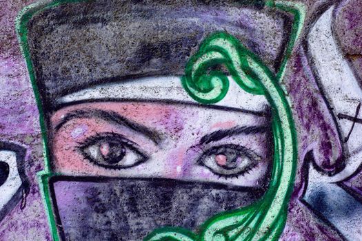 Portrait of woman face covered by niqab islamic dress while leaving beautiful eyes uncovered sprayed as street graffiti on wall