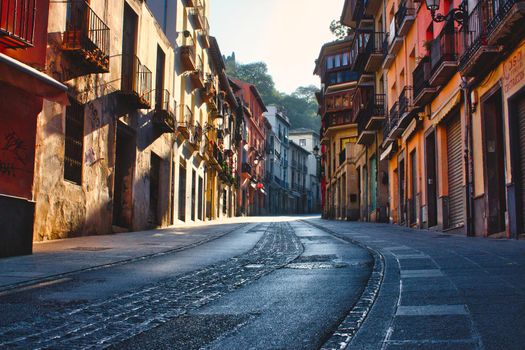 A moody and picturesque view of a street in Granada, Spain, winding uphill with tall buildings on either side