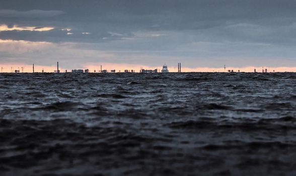the city of Kronstadt on the sea horizon in cloudy weather, the outlines of the city are blurred by the heat from the water, tall buildings and structures against the background of the sunset sky. High quality photo