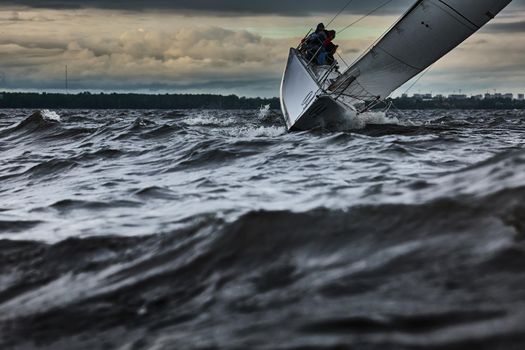 Sailboat in sea at stormy weather, stormy clouds sky orange sky, sail regatta, reflection of sail in the water, bigl waves of water, . High quality photo