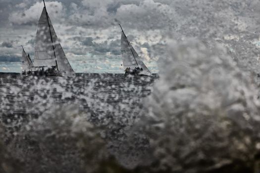 Russia, St. Petersburg, 17 June 2022: Splashes of water in sailing regatta, teamwork in sailing yacht at stormy weather, hot pursuit, clouds sky . High quality photo