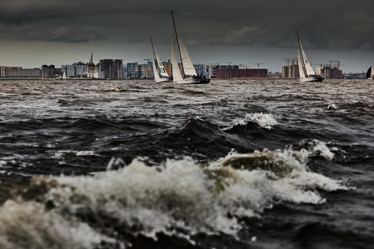 Russia, St. Petersburg, 17 June 2022: The residential complex under construction on the embankment of the Neva River on Vasilievsky island in stormy weather, construction cranes, sailing yachts. High quality photo