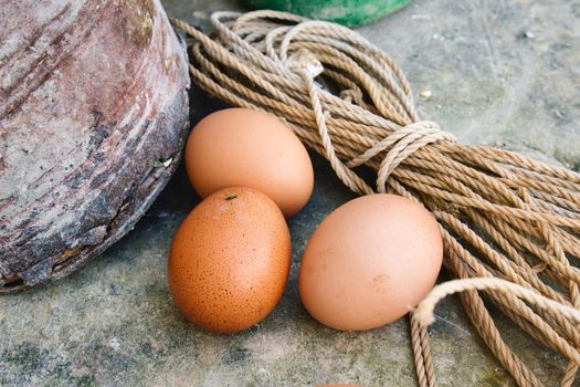 A small group of three brown hen's eggs on the floor in a rustic farmyard
