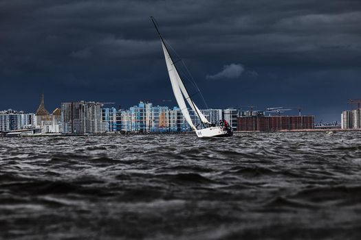 Russia, St. Petersburg, 17 June 2022: The residential complex under construction on the embankment of the Neva River on Vasilievsky island in stormy weather, construction cranes, sailing yachts. High quality photo