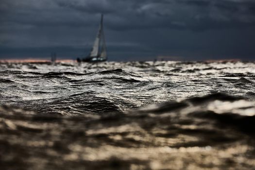 Sailboat in sea at stormy weather, blurred background, stormy clouds sky, sail regatta, reflection of sail in the water, big waves of water. High quality photo