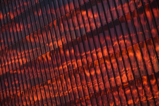 The glass and iron facade of huge skyscraper at sunset, steel, orange color, reflection of sun. High quality photo