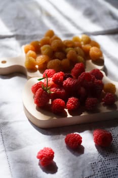 Two handfuls of fresh red and yellow raspberry on white wooden kitchen boards, sselectivew focus, hard light.