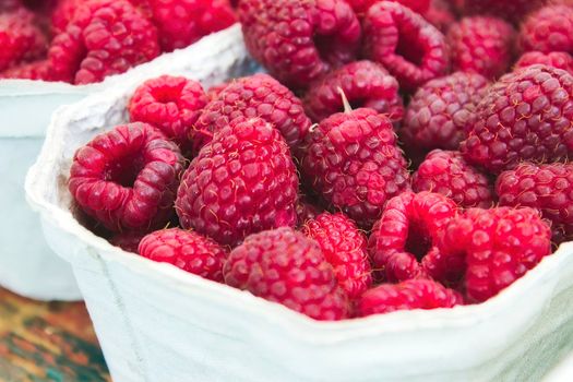 Close-up of a container of fresh, red, ripe raspberries at an open-air food market