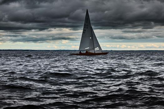 Sailboat in sea at stormy weather, stormy clouds sky orange sky, sail regatta, reflection of sail in the water, bigl waves of water, . High quality photo