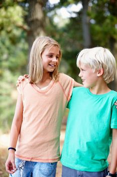 Young siblings standing outdoors with arms around.